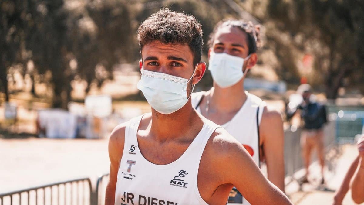 Two athletes wearing facemasks prepare for an outdoor race event, showcasing pandemic precautions.
