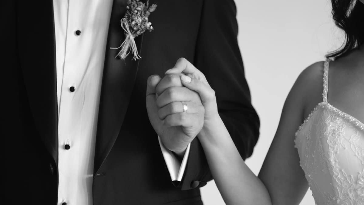 Black and white close-up of a bride and groom holding hands, symbolizing love and commitment.