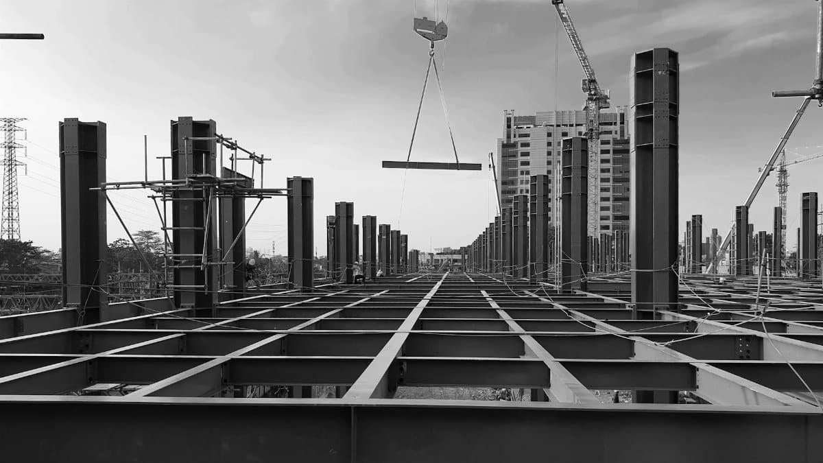 Black and white view of a modern urban construction site in Indonesia with steel beams and cranes against a cloudy sky.