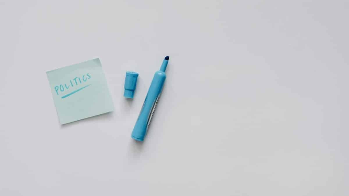 A flat lay of a blue marker and sticky note with 'politics' on a white surface.