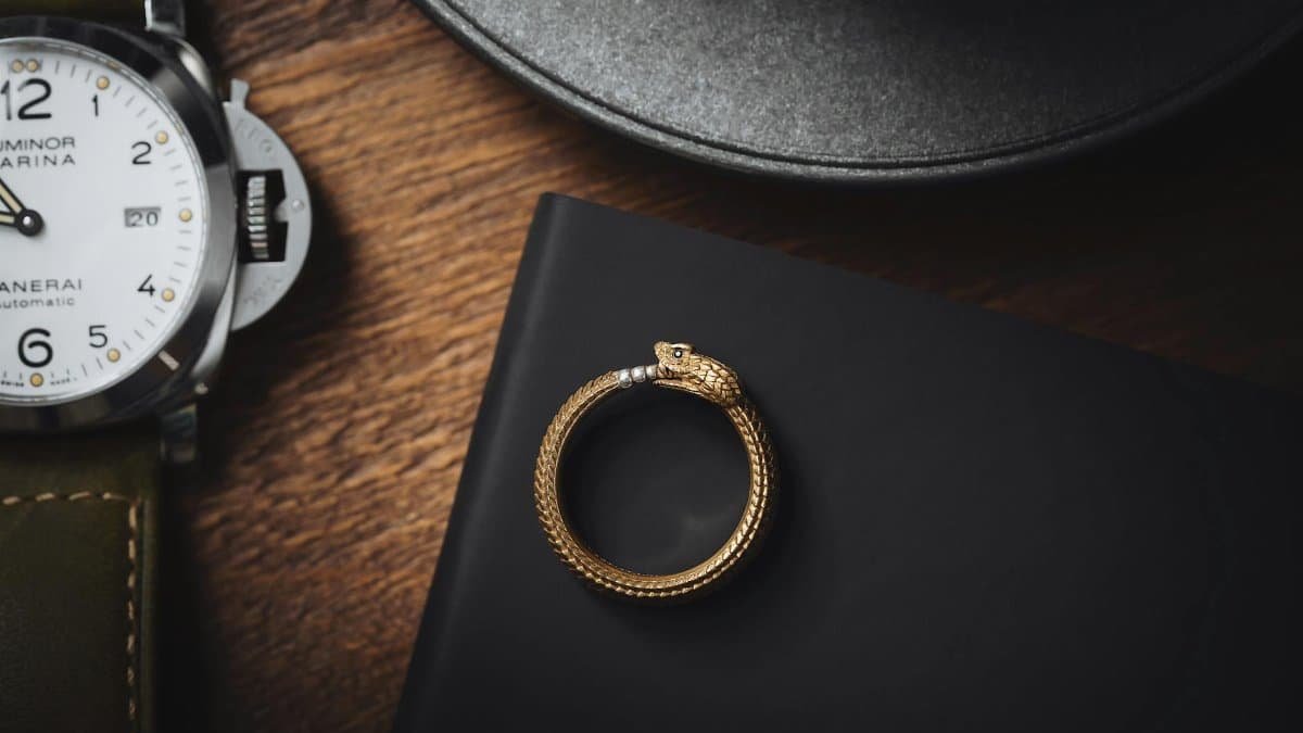 Close-up of a stylish snake ring and luxury wristwatch on a dark wooden surface.