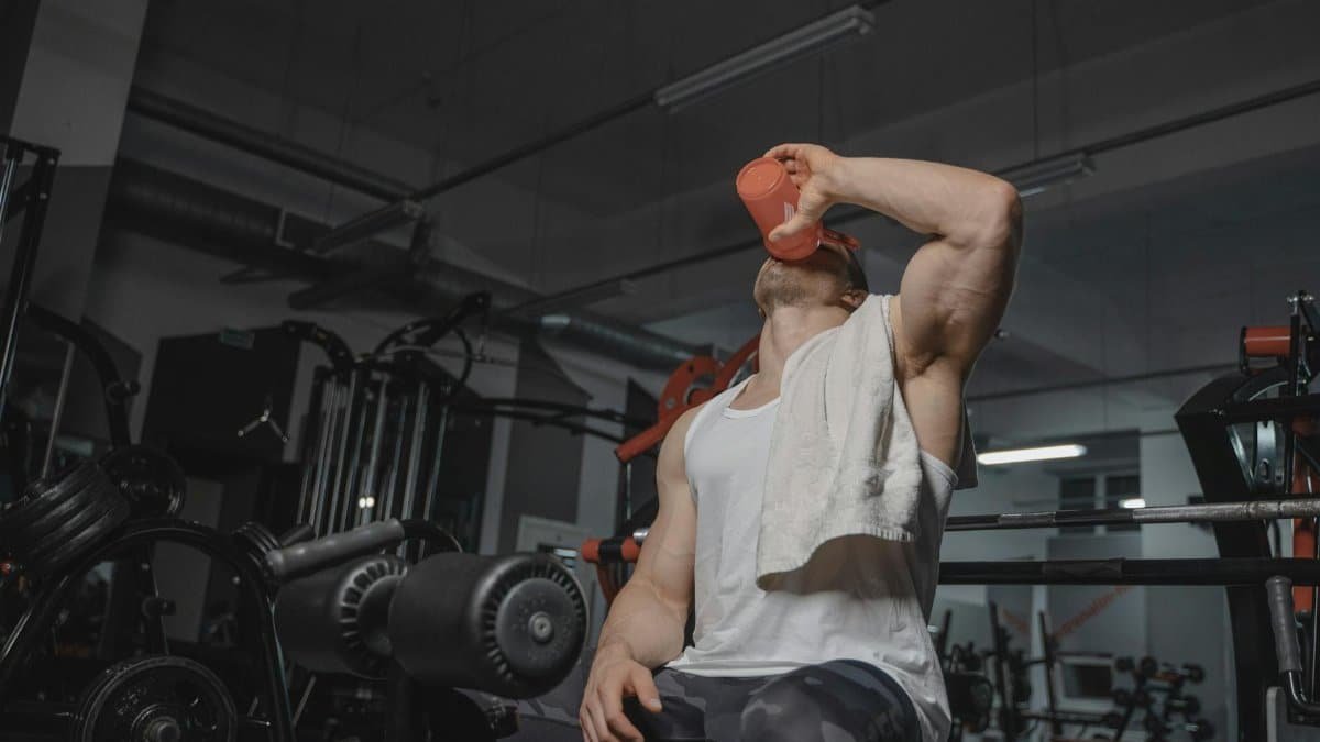 Strong man in gym drinking protein shake, emphasizing fitness and muscularity.