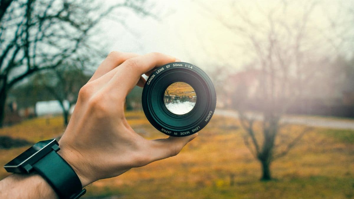 Close-up of a hand holding a 50mm camera lens outdoors, focusing through the lens.