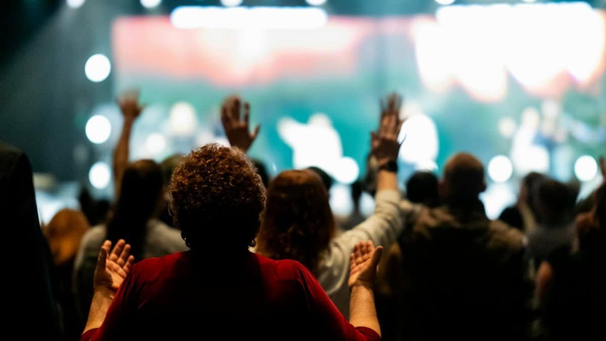 A diverse group of people worshiping with raised hands at an indoor event.