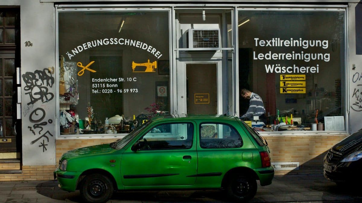 A green car parked outside a tailor shop in Bonn, Germany.