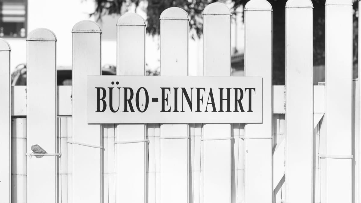 Black and white photo of an office entrance sign on a white picket fence with a tranquil setting.