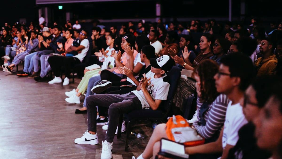A diverse crowd seated in an auditorium applauds a live performance.