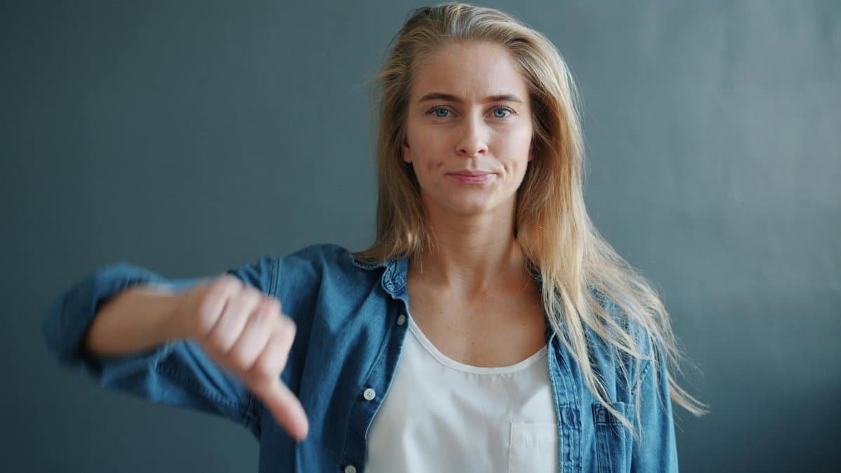 Confident young woman displaying a thumbs down sign against a neutral background.