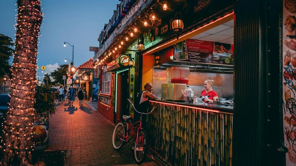 Bustling Miami street at night with a lively food stall and colorful lighting.