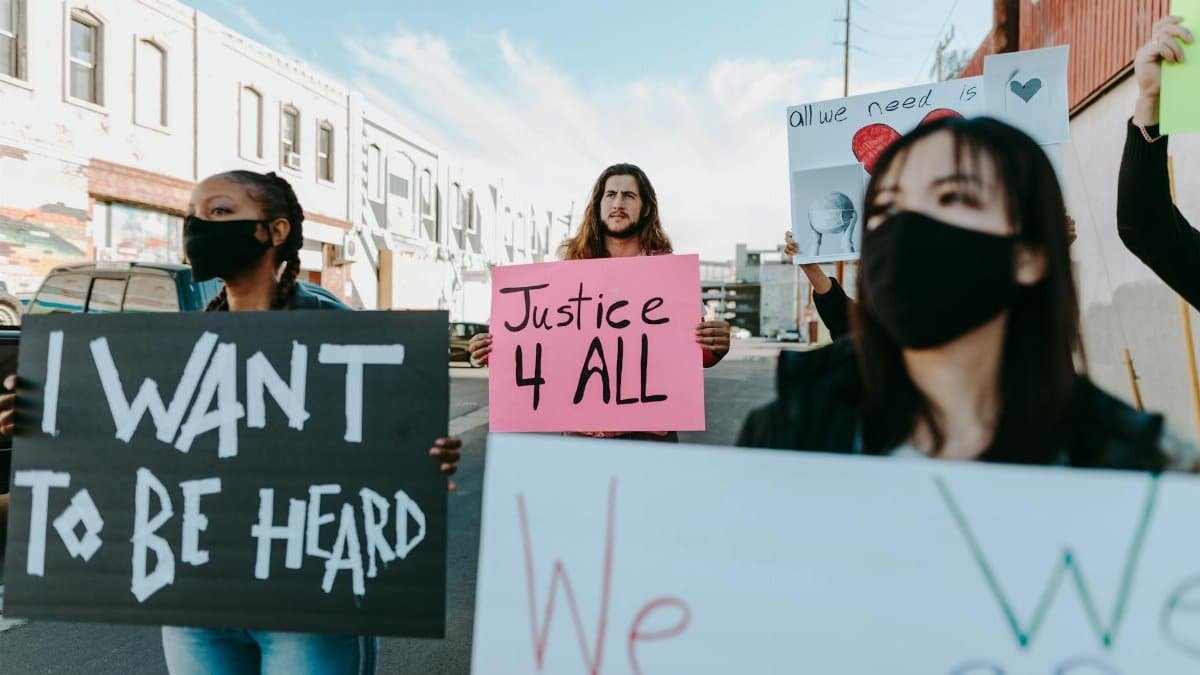 A diverse group of masked protesters holding signs that demand justice in an outdoor rally.