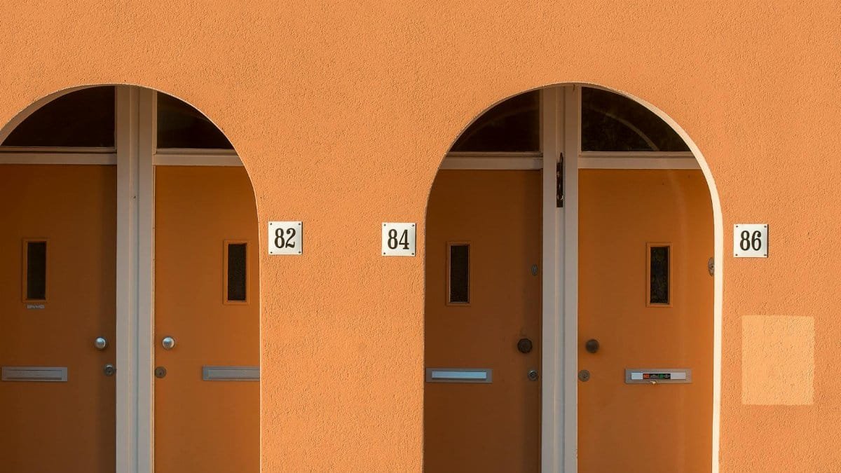Stylish orange doors with arched frames and house numbers 82, 84, 86 on a sunny wall.