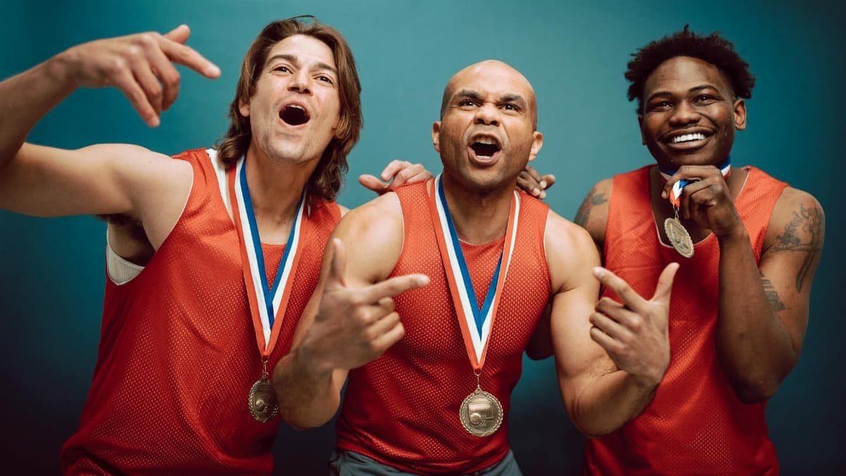 Three male athletes in red jerseys celebrating with medals indoors.