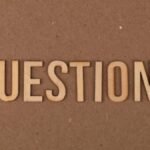 Wooden letters spelling the word "QUESTIONS" on a cardboard background, providing a neutral copyspace.