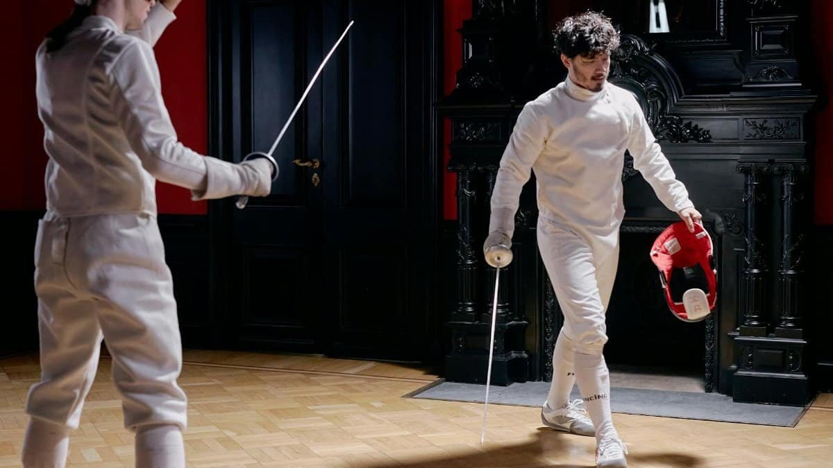 Two fencers in action during an indoor training session with ornate decor.