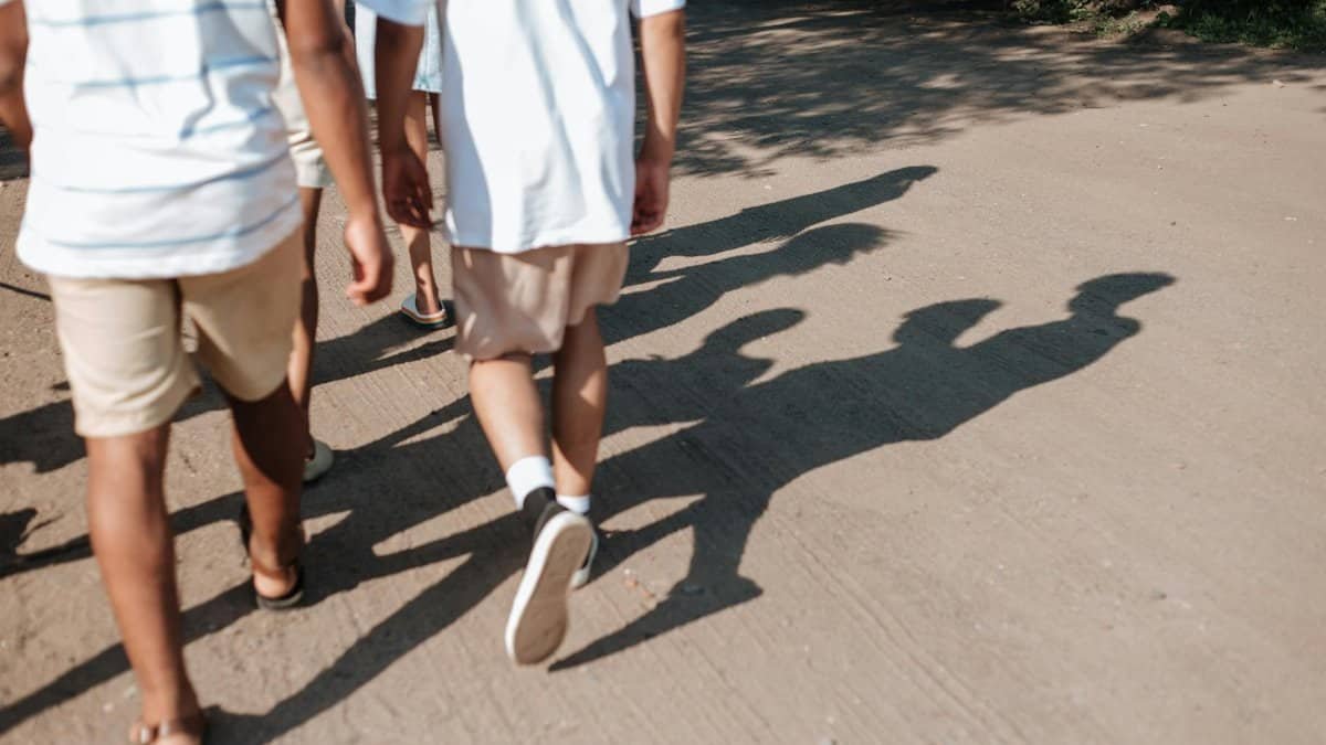 A group of teenagers walking on a sunlit dirt path during summer, casting long shadows.