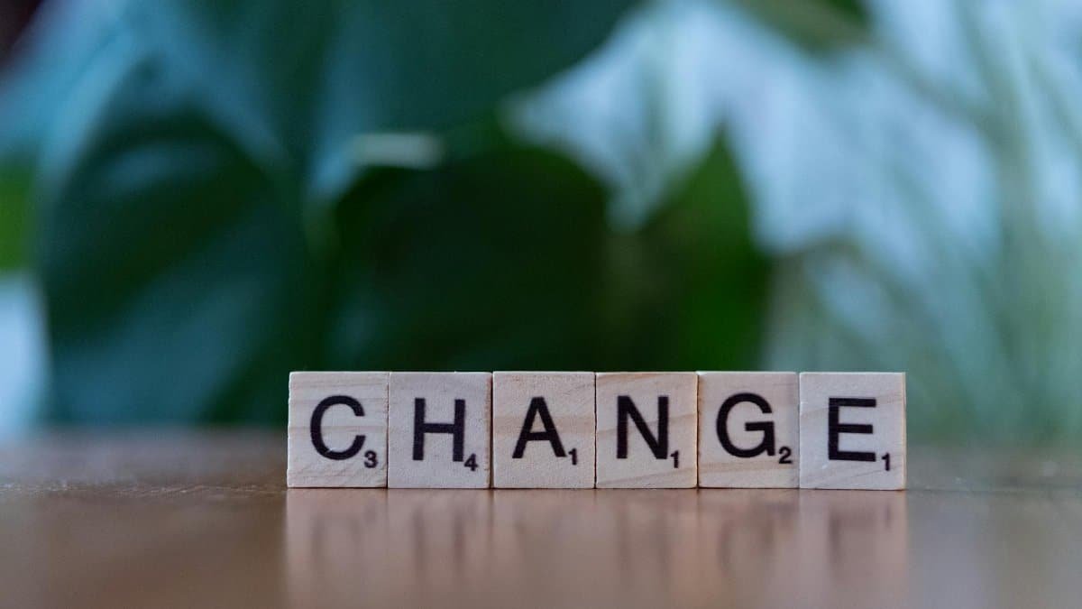 Scrabble tiles spelling 'CHANGE' on a wooden surface with a blurred green background.