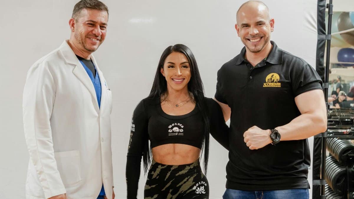 Three people smiling and standing in a fitness studio, capturing a friendly and energetic moment.