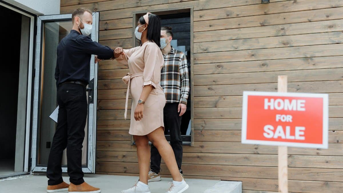Masked real estate agent greets clients with elbow bump outside a home for sale.