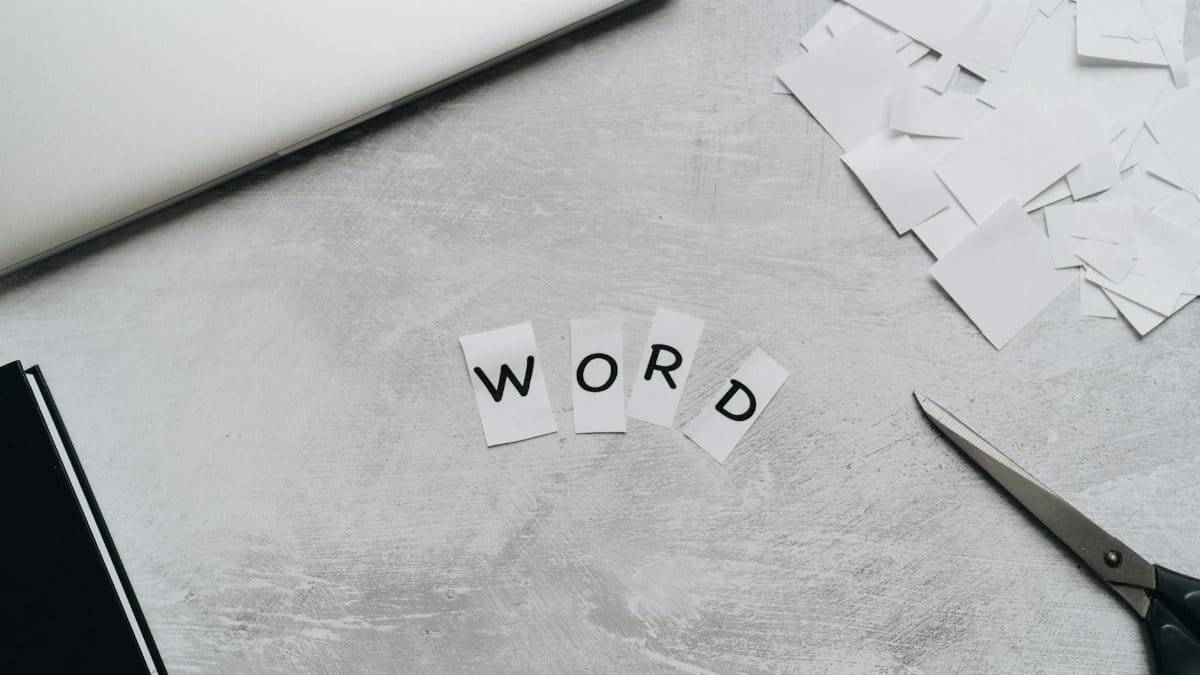 Top view of a workspace with scattered paper letters spelling 'WORD', next to a laptop and scissors.