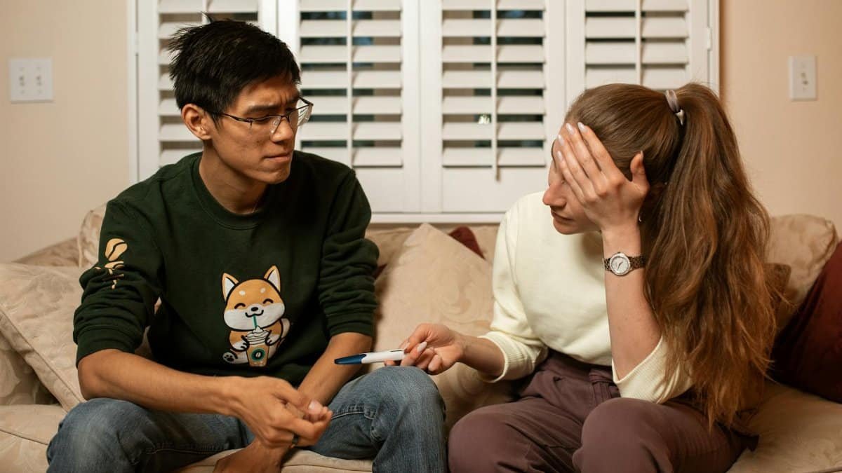 A couple on a couch reacts emotionally to a pregnancy test result, signaling life-changing news.