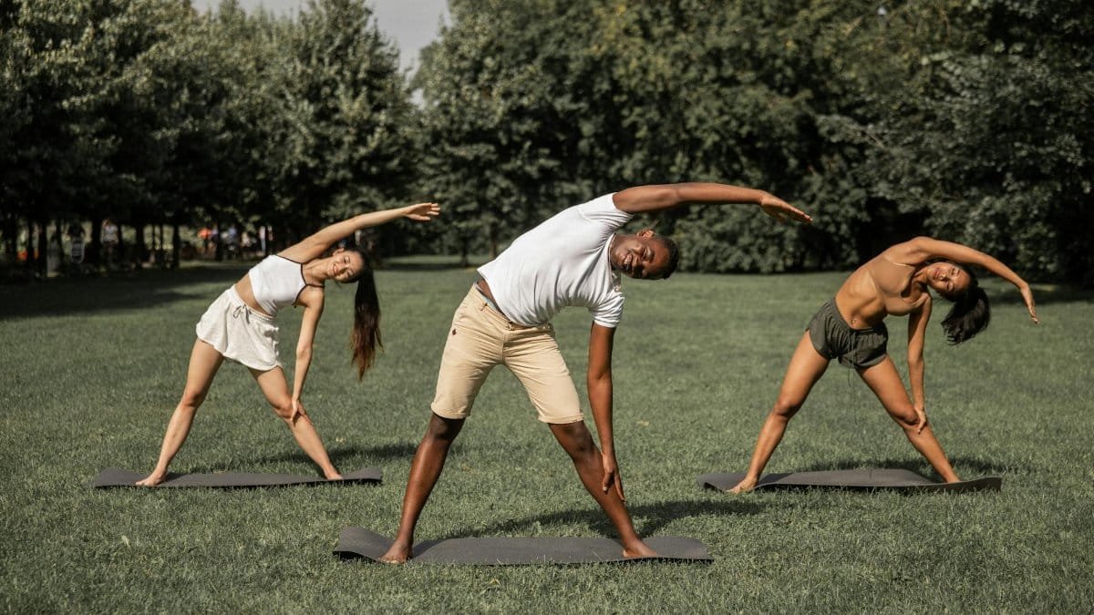 Group of diverse people in activewear stretching body while practicing Parivrtta Trikonasana in summer park