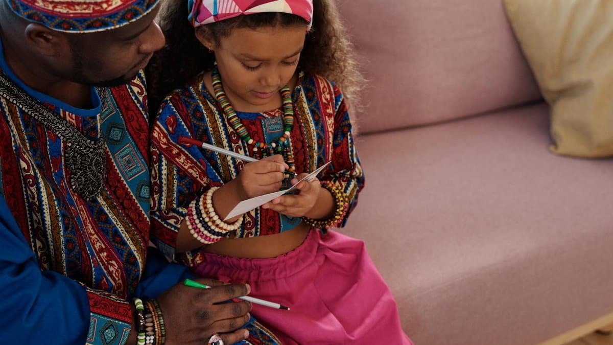 Father and daughter spending quality time indoors, wearing traditional dashiki outfits.
