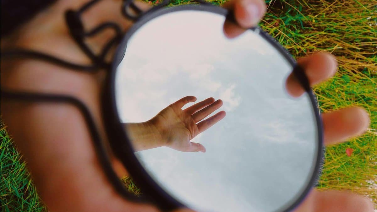 A hand reflecting in a pocket-size mirror held over green grass. Surreal outdoors image.