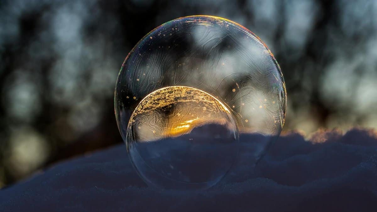 Close-up of a frozen soap bubble reflecting golden light on a snowy surface outdoors.
