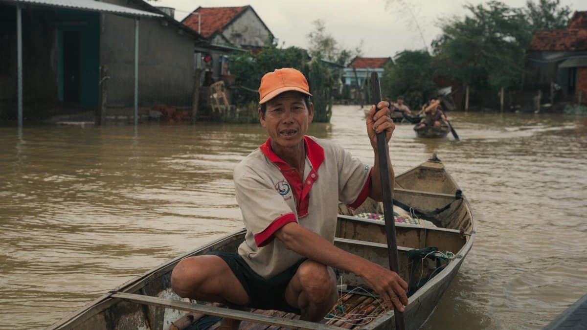 An adult man navigates a wooden boat through a flooded village in Phú Yên, Vietnam, showcasing resilience.