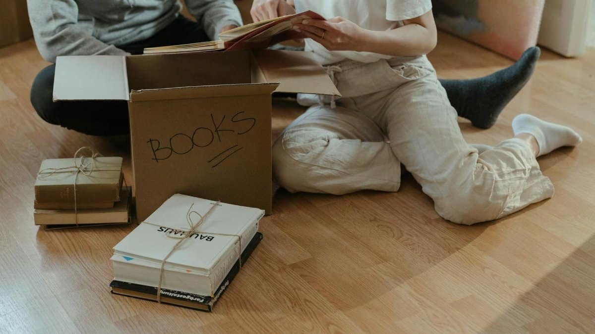 A couple sitting on the floor, unpacking books from cardboard boxes in their new apartment.