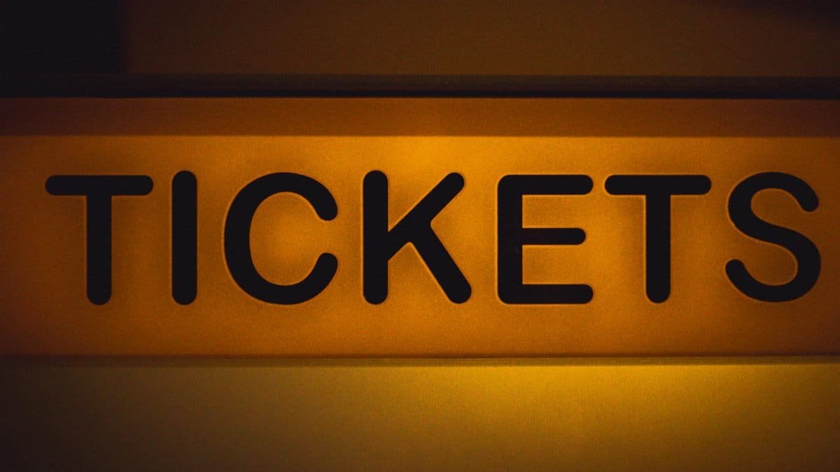 Close-up of an illuminated yellow ticket sign against a dark background.