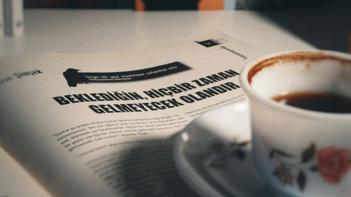 A porcelain coffee cup on a table with a Turkish magazine page in soft lighting.