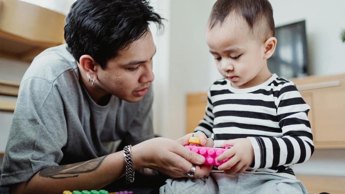 A father and son enjoy quality time together indoors, playing with colorful toys.