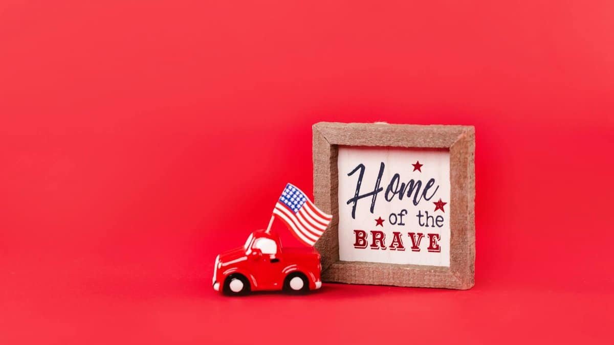 A miniature car with an American flag and 'Home of the Brave' sign on a red background.