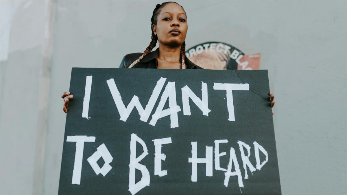 A young woman holds a protest sign outdoors, advocating for being heard.