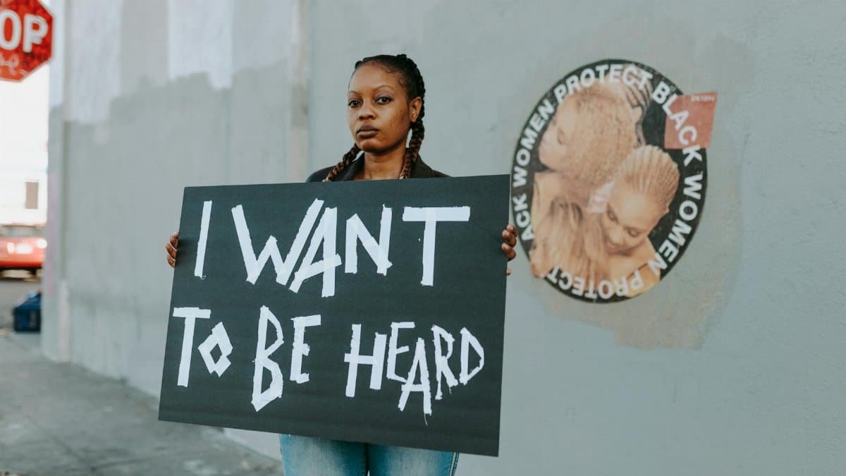African American woman at protest holding a sign reading 'I Want to Be Heard.'