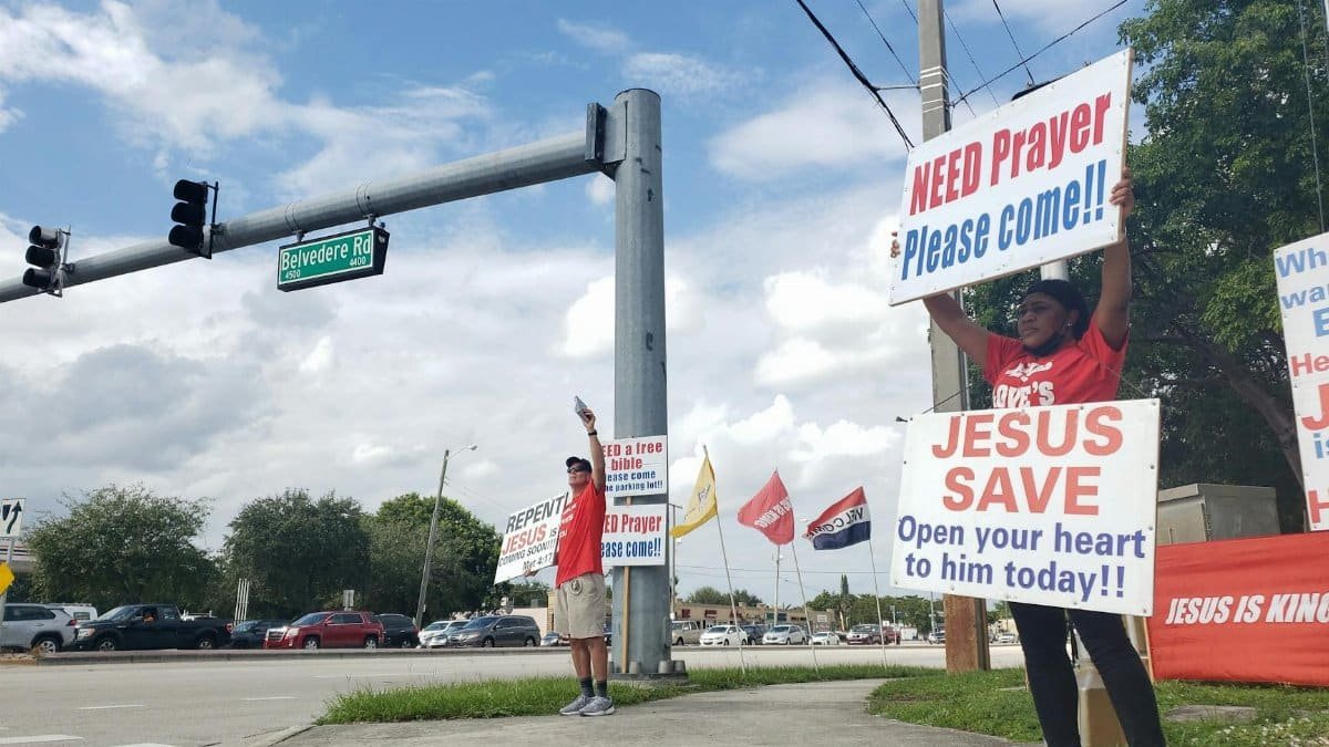 Group holding religious signs promoting prayer and faith on a city street corner.