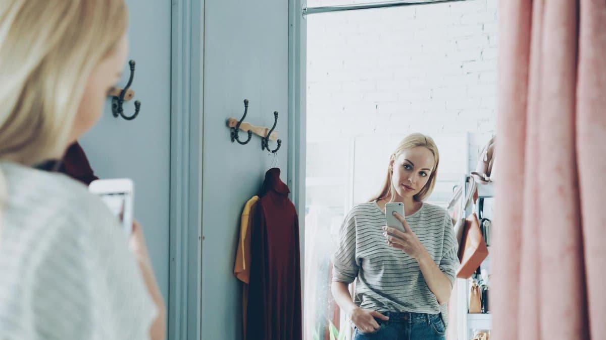 Fashionable woman takes a selfie in a stylish changing room setting, capturing her reflection.