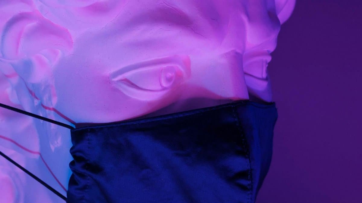 White sculpture of Apollo with medical mask on face in bright neon light on purple background