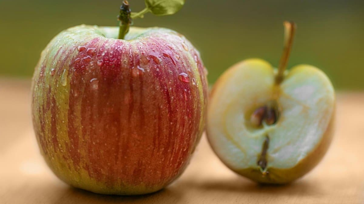 Close-up of a fresh red apple with dew, beside a sliced half on a wooden surface.