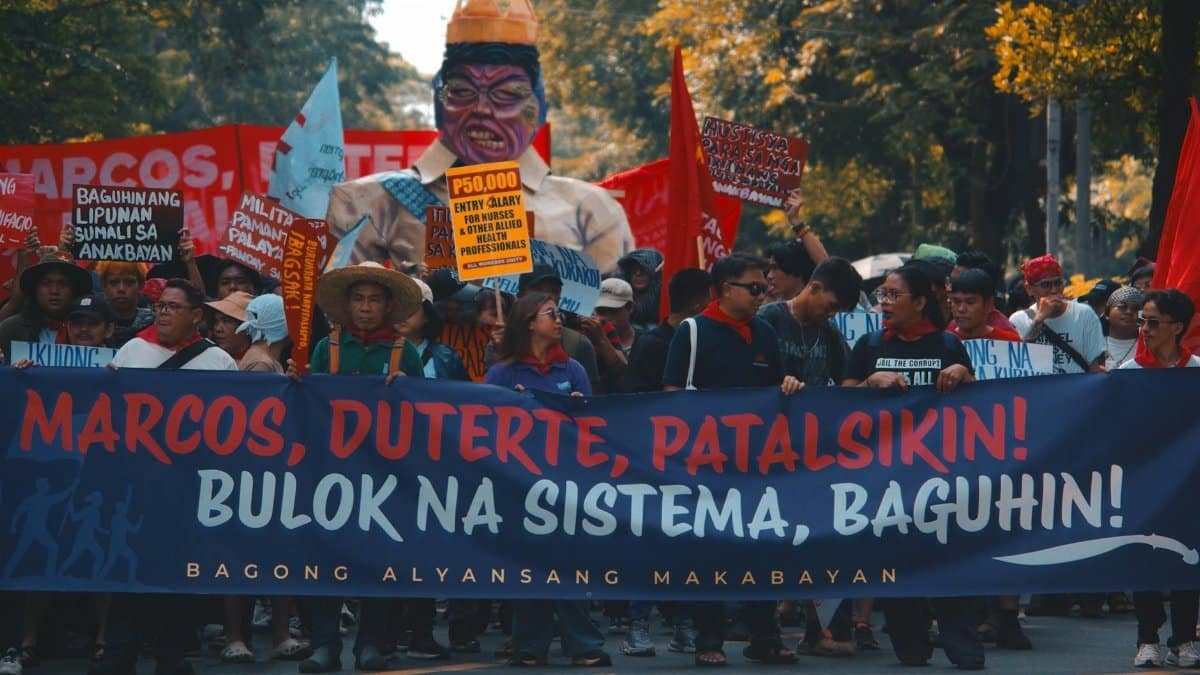 Street protest with demonstrators holding political banners and signs demanding change.