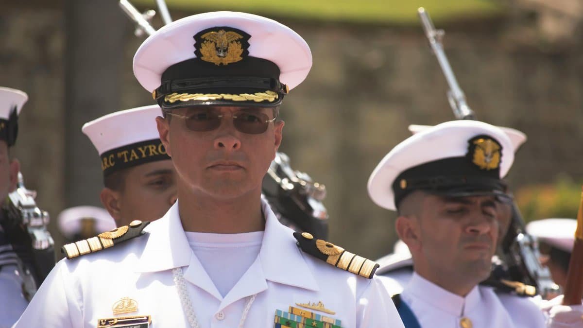 Group of navy officers in white uniforms participating in a formal ceremony outdoors.