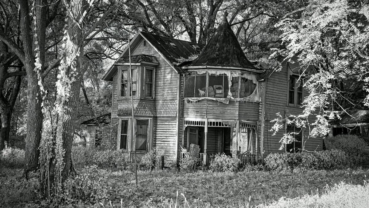 An eerie, abandoned Victorian house amidst trees in Weaver, MN, captured in black and white.