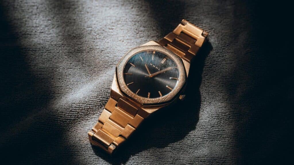 Close-up of a gold analog watch with a sleek design, artfully lit to highlight its elegance and style.