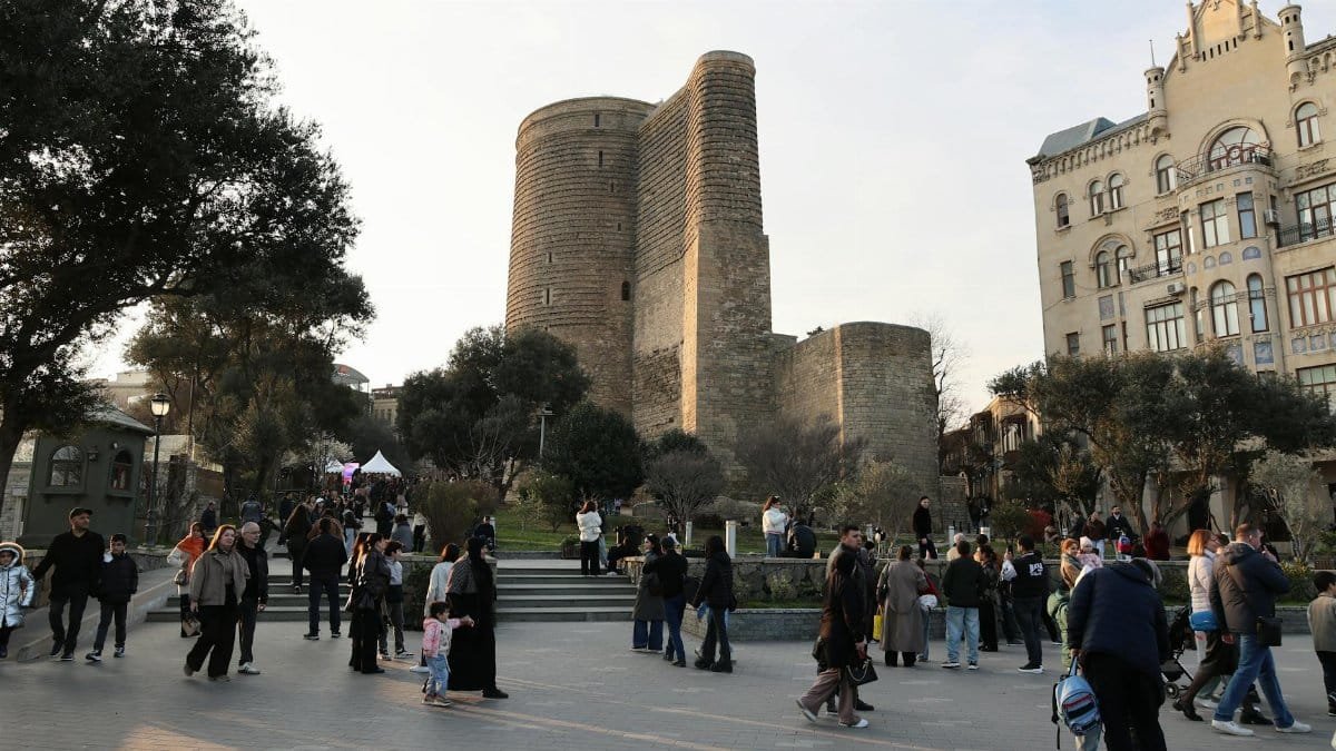 People gathering at the historic Maiden Tower in Baku on a sunny day.