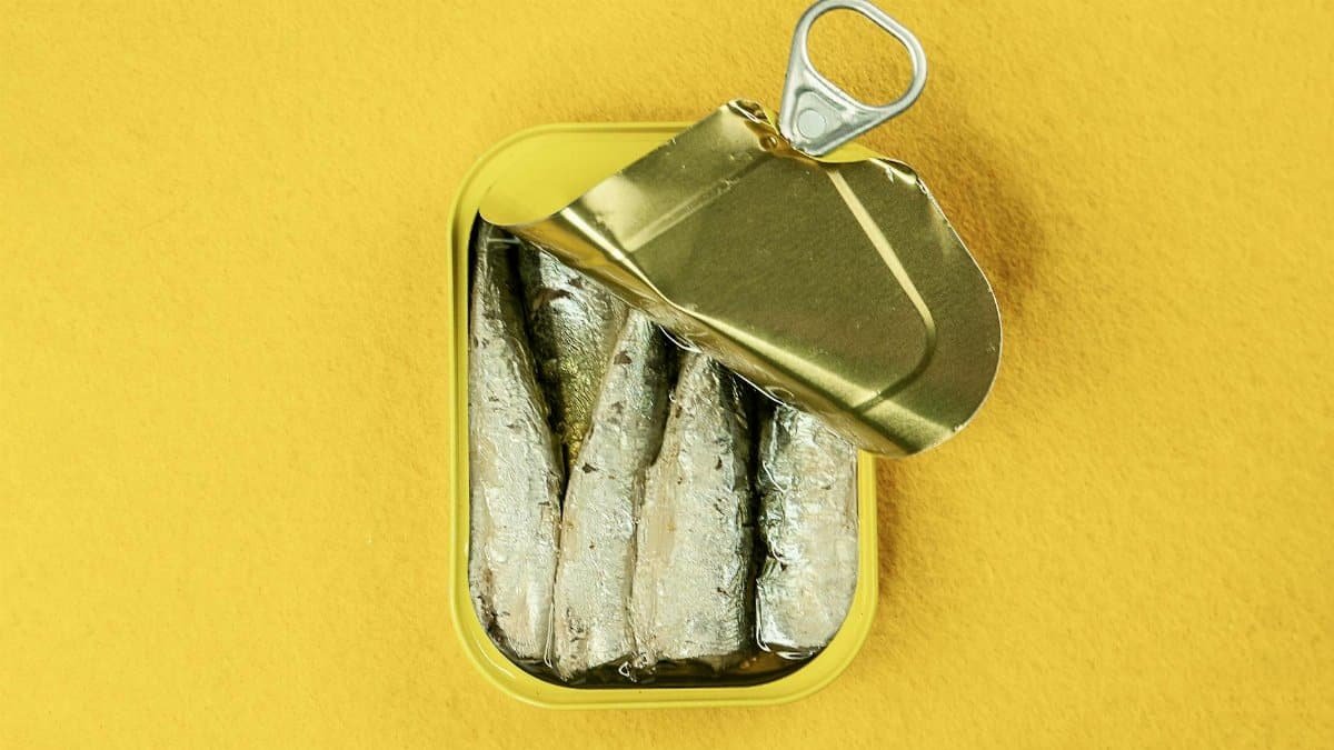 Metal can of sardines opened, revealing fish against a bright yellow background.