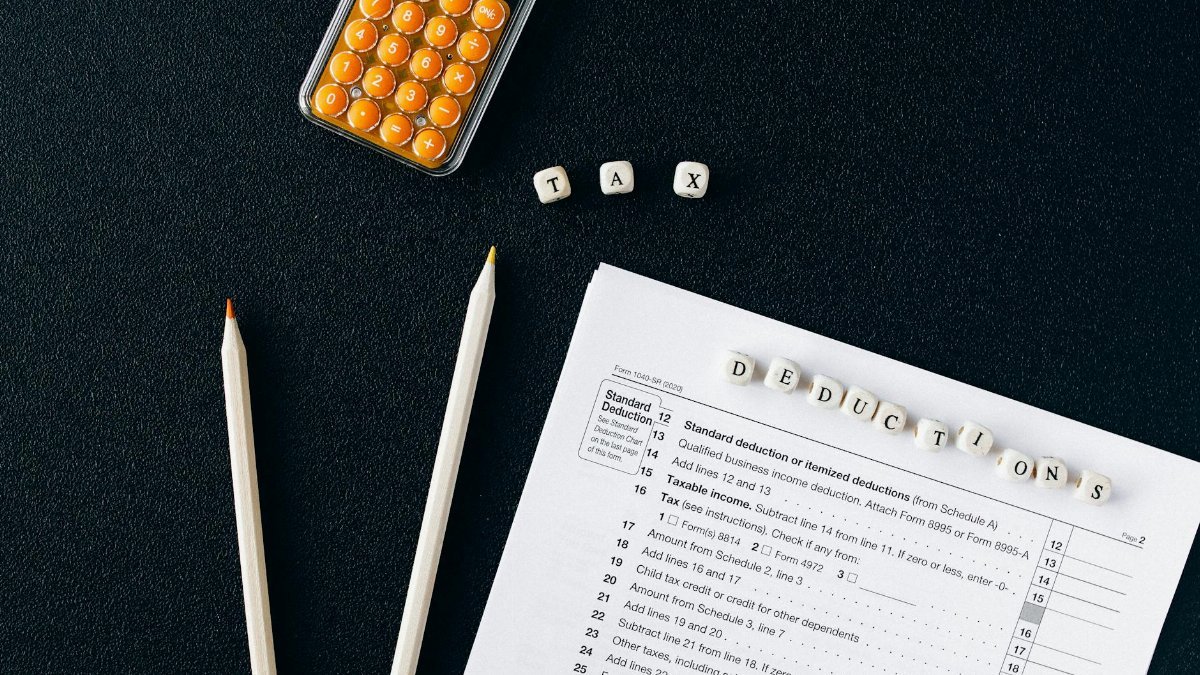 Flat lay of tax form, pencils, and calculator on black background, emphasizing tax deductions.