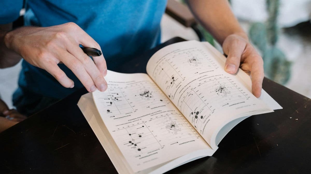 Person flipping through a textbook, examining pages with scientific graphs. Ideal for educational contexts.