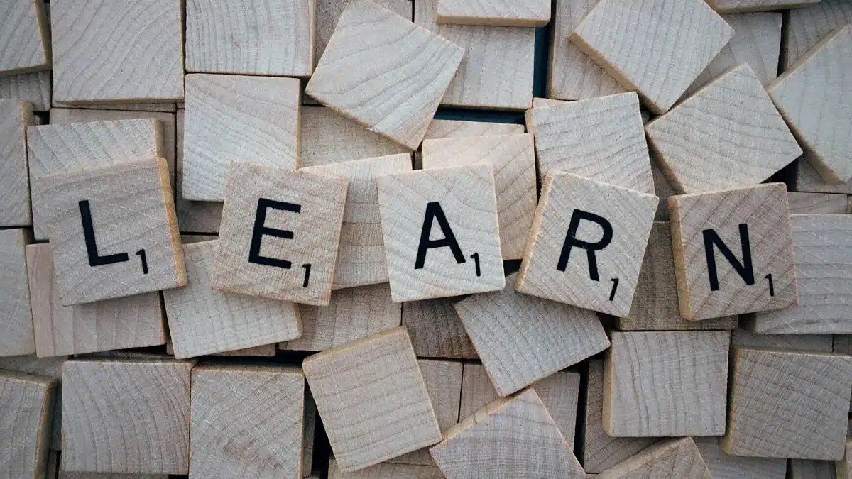Wooden letter tiles arranged to spell 'learn' on a background of scattered tiles.