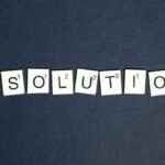 Scrabble tiles spell 'RESOLUTIONS' on a textured dark blue background, capturing a New Year theme.